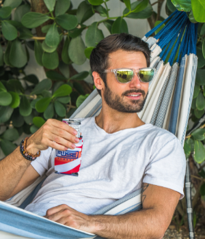 Man in a hammock holds a beer and looks into distance