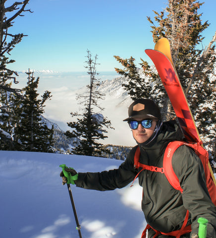 Man carrying red skis and wearing blue mirrored sunglasses in snow
