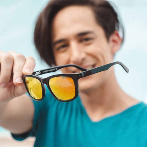 Man holding out bright orange mirrored sunglasses