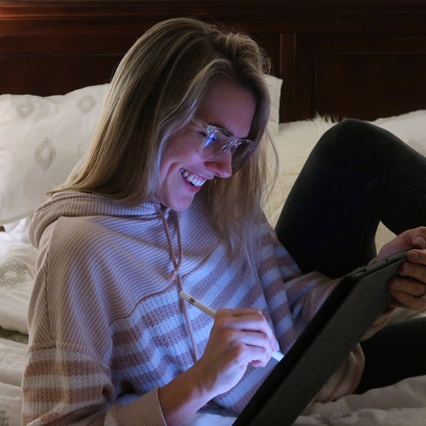 Blonde woman in dark room using ipad wearing blue light lenses