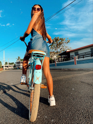 woman in dress riding a blue bike in sunglight down street