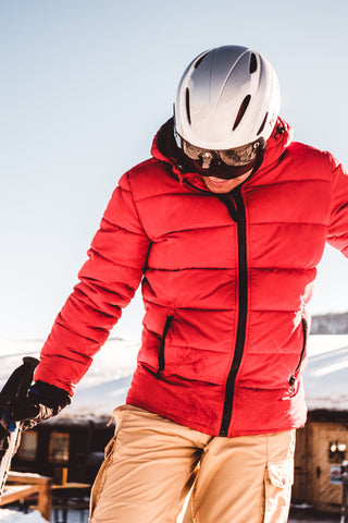 man in red puffy jacket with helmet and sunglasses on snowboarding