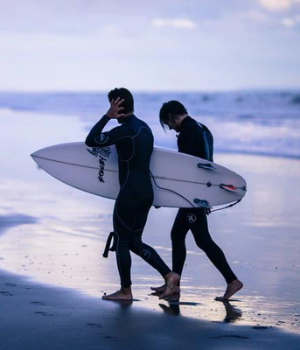 Two surfers walk on a beach at dusk with surfboards in hand