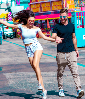 Man and woman skip through carnival with shades on