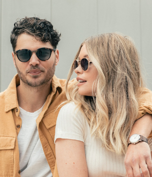 Man and woman embrace from side while wearing neutral tone glasses