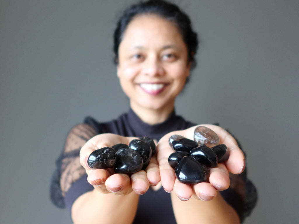 sheila of satin crystals holding black and brown protection tumbled stones