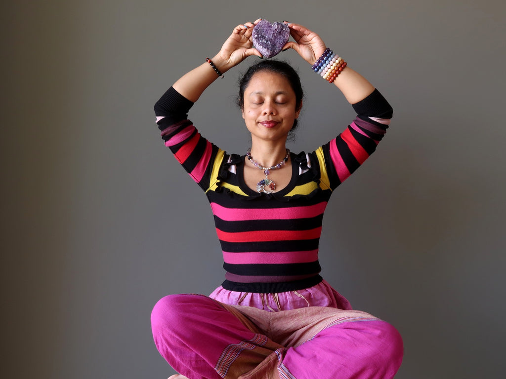 sheila of satin crystals meditating with a amethyst geode heart at her crown chakra