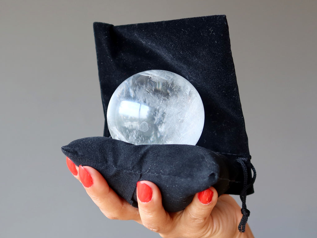 holding clear quartz sphere on black pillow