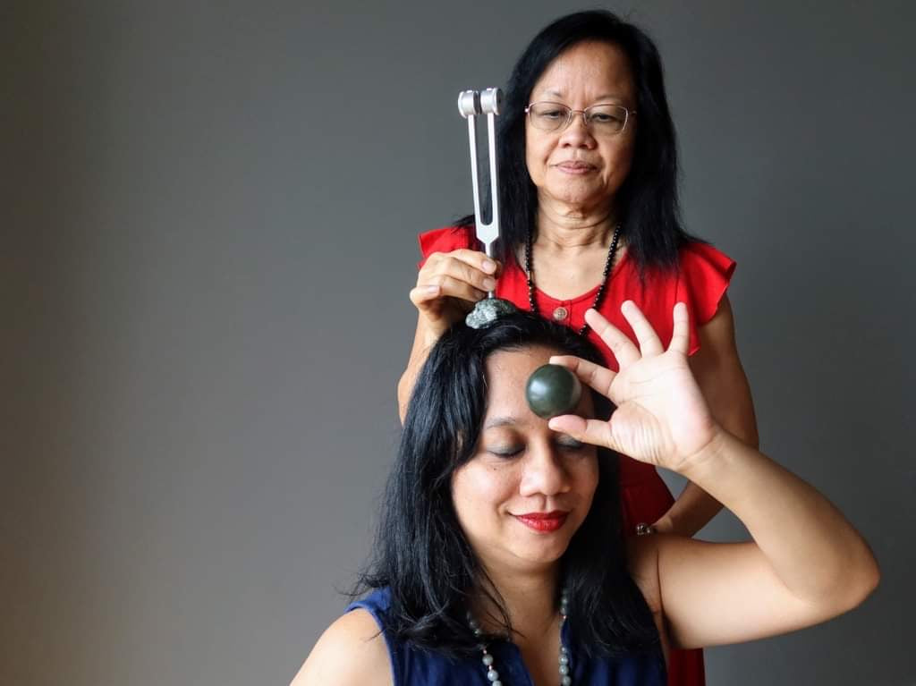 Healer using tuning fork on client with Jade on third Eye chakra