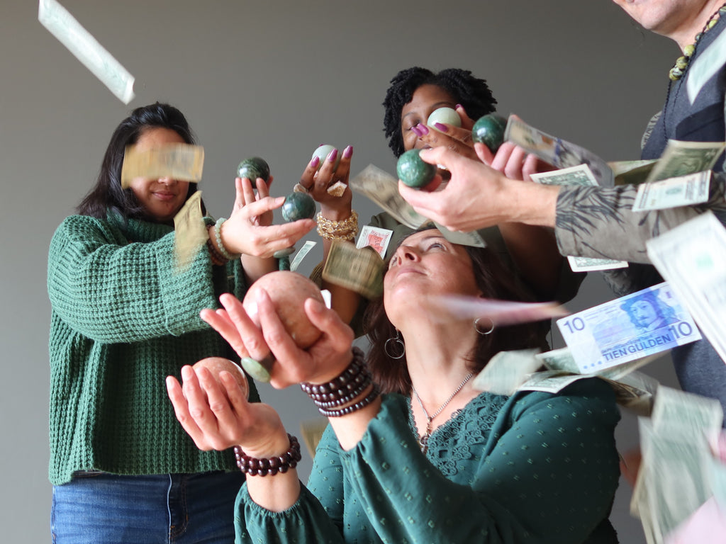 woman meditating with pink aventurine spheres surrounded by three people holding green aventurine spheres as money falls around them