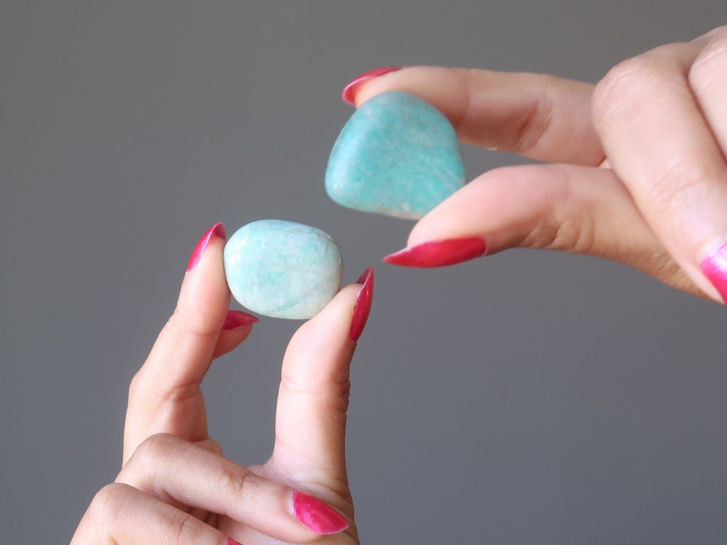 hands holding two blue amazonite tumbled stones at satin crystals