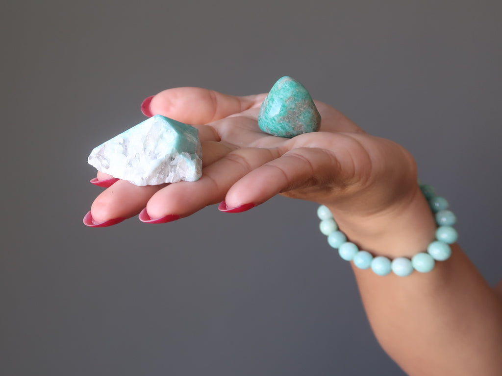 hand wearing an Amazonite bracelet holding a rough and a tumbled Amazonite stone