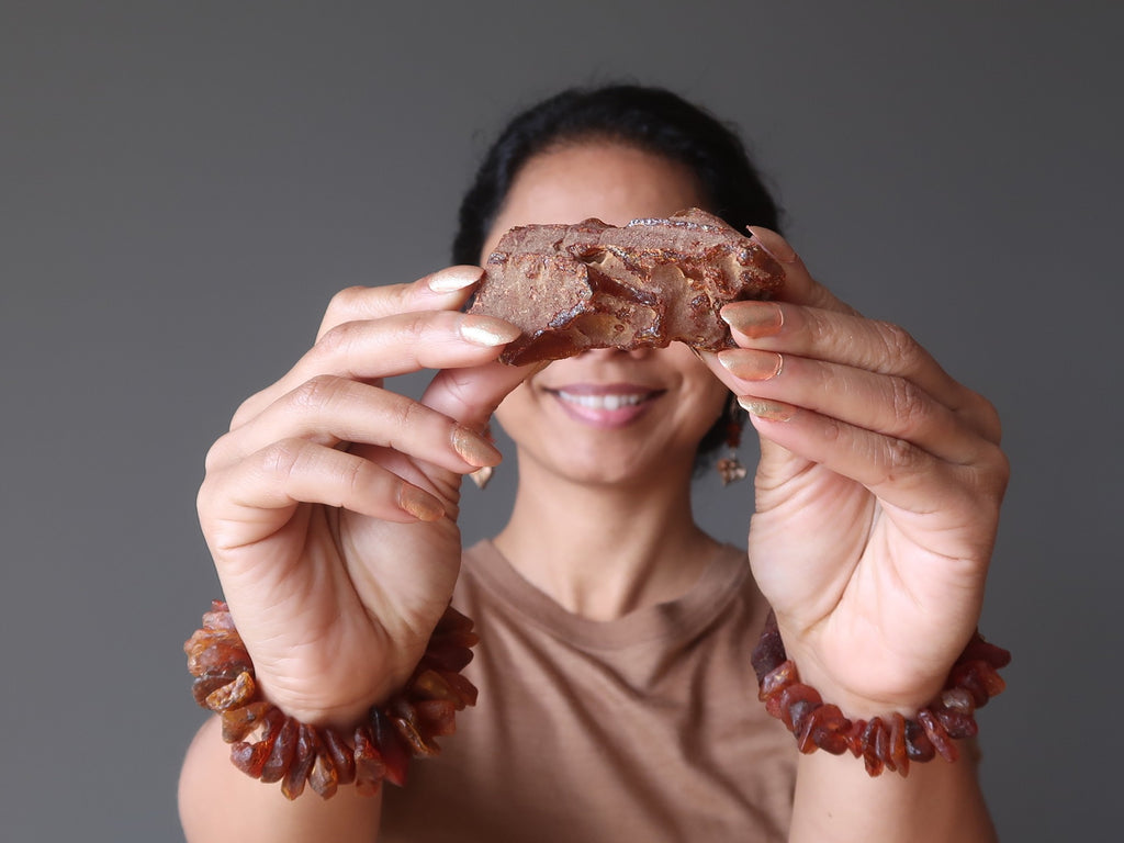 sheila of satin crystals holding up a raw amber gemstone wearing two chunky beaded amber stretch bracelets