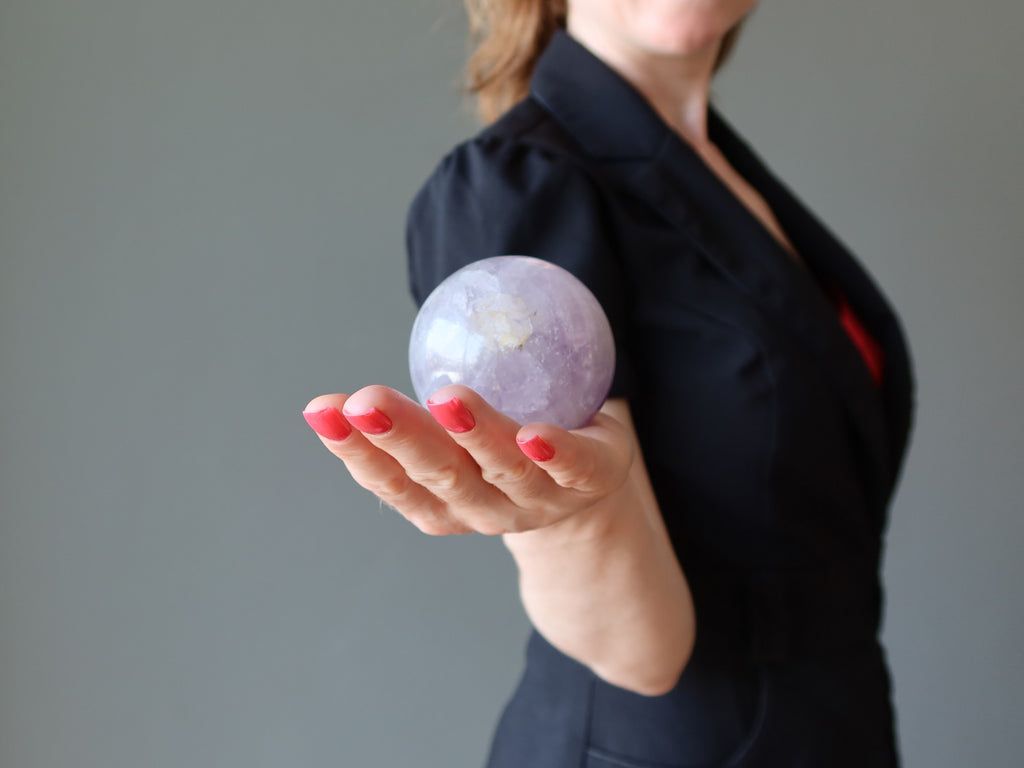 female holding a light purple amethyst sphere