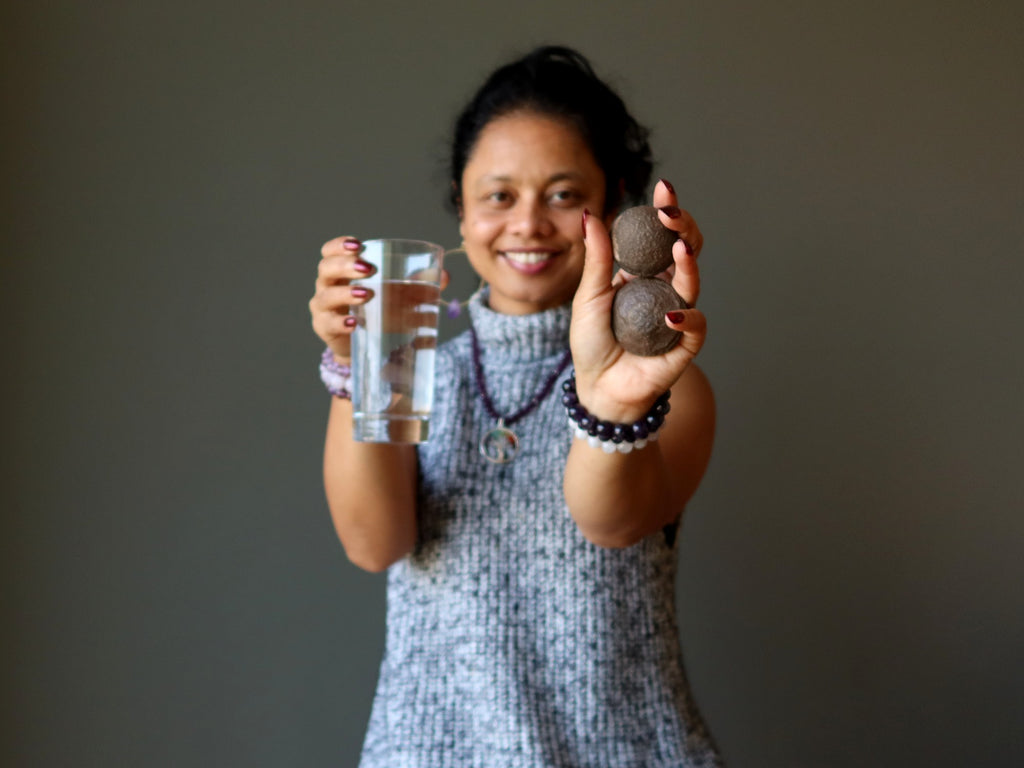 sheila of satin crystals holding glass of water and a pair of moqui marble stones for post-meditation grounding