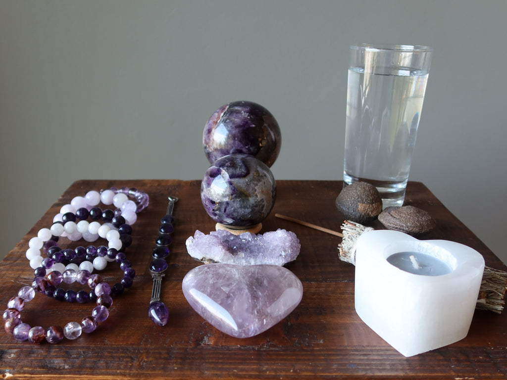 table of amethyst jewelry, stones, water, moqui marbles and candle for meditation