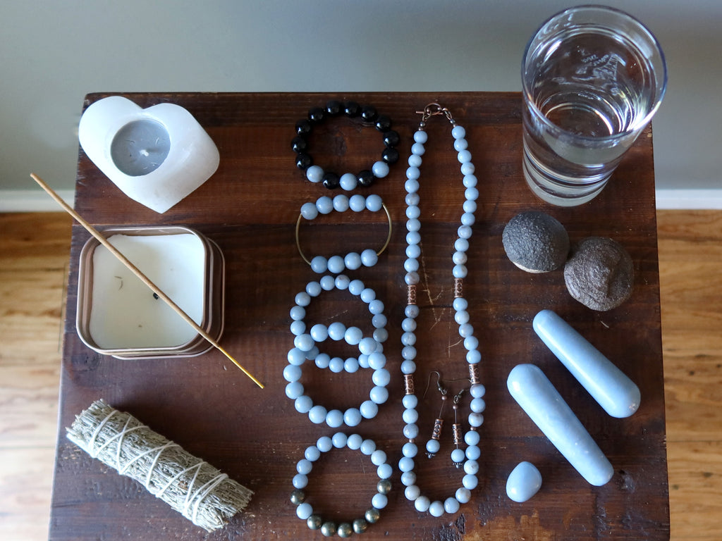 table with angelite jewelry, stones, candles, sage, water, moqui stones