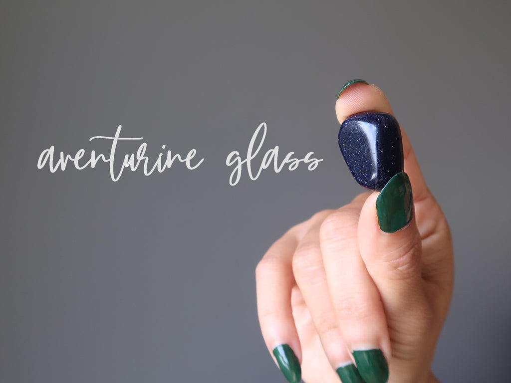 hand holding a navy blue goldstone aventurine glass tumbled stone