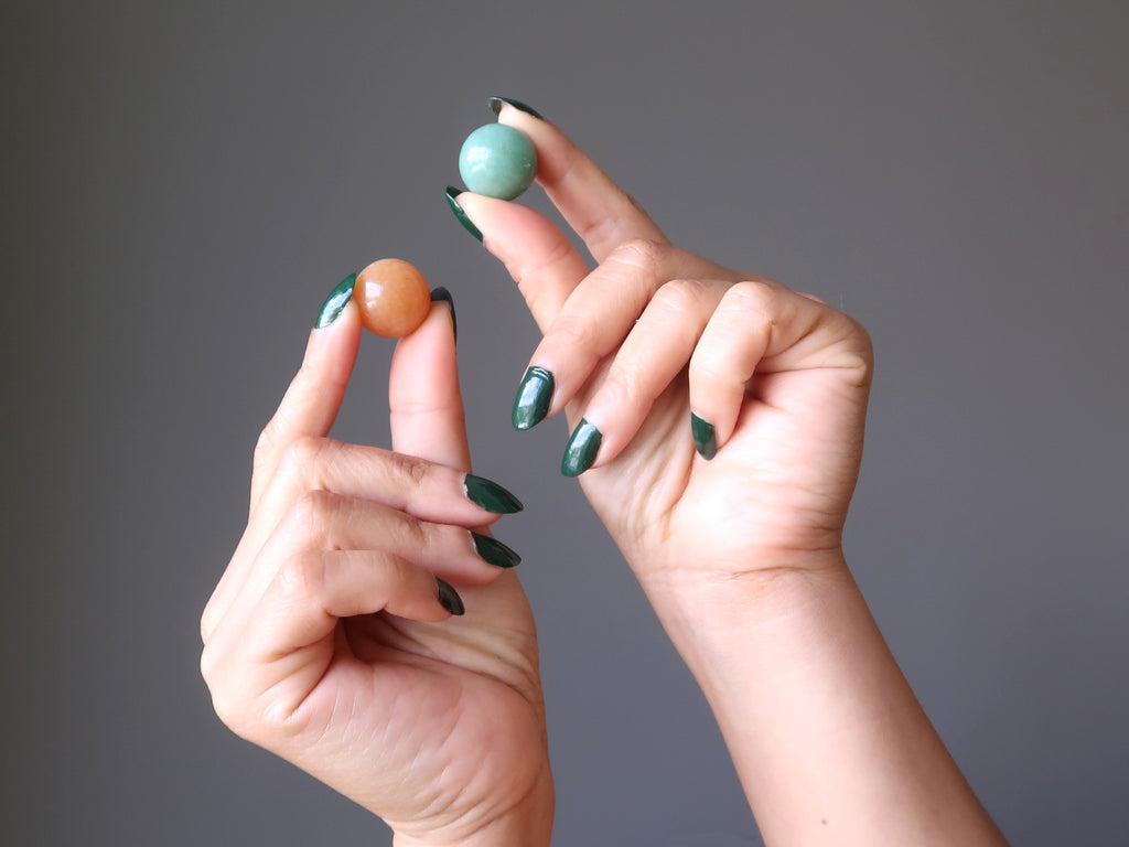 hands holding a red orange aventurine marble and a green aventurine marble