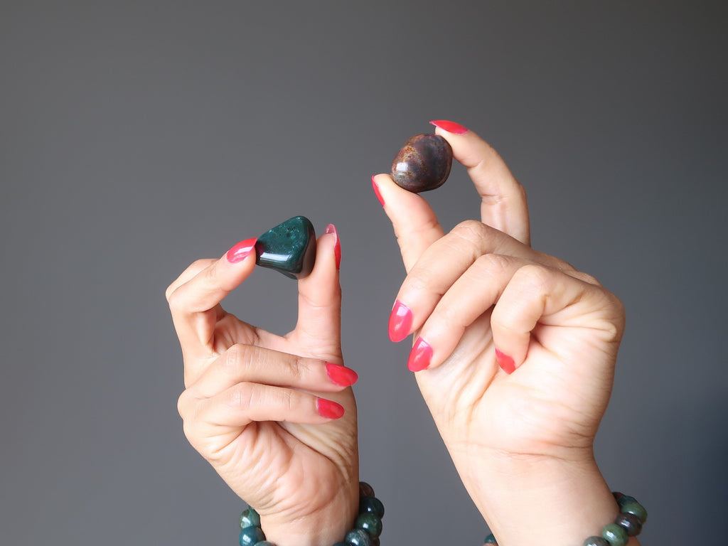 hands wearing bloodstone stretch bracelets holding up a green and red tumbled stones