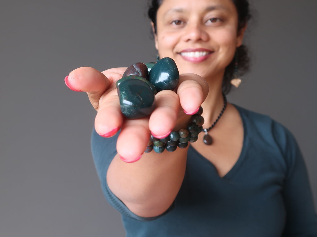 sheila of satin crystals holding a hand full of green and red bloodstone tumbled stones`