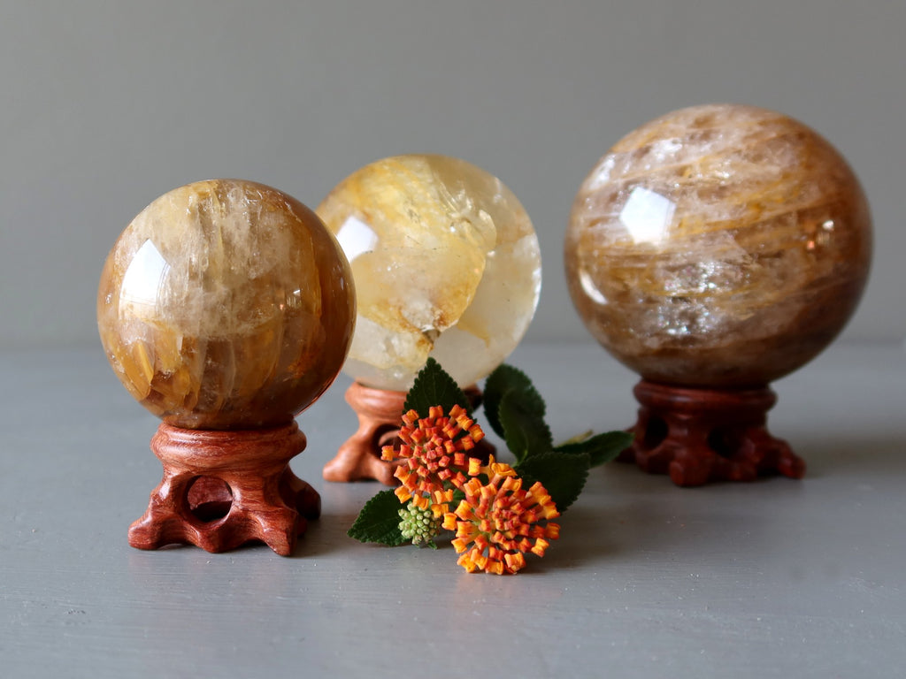 golden healer quartz spheres on wood stands with orange flowers