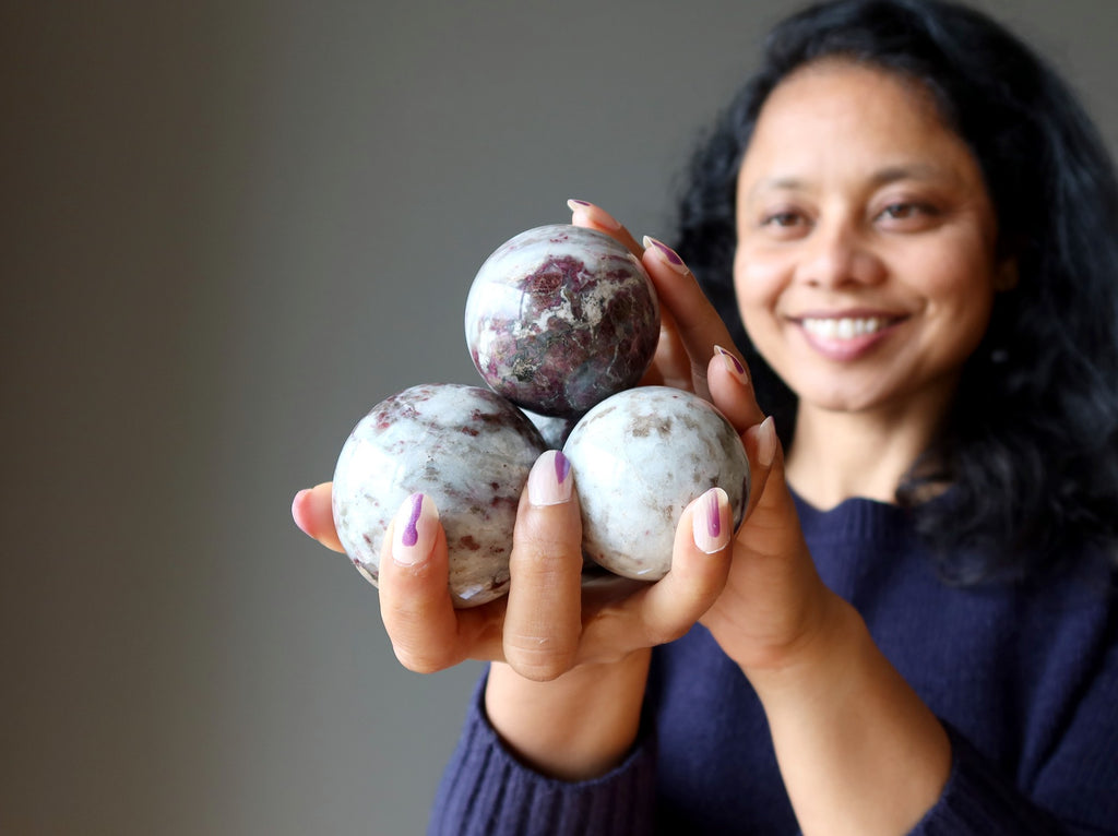 sheila of satin crystals holding up a pile of tourmaline quartz spheres