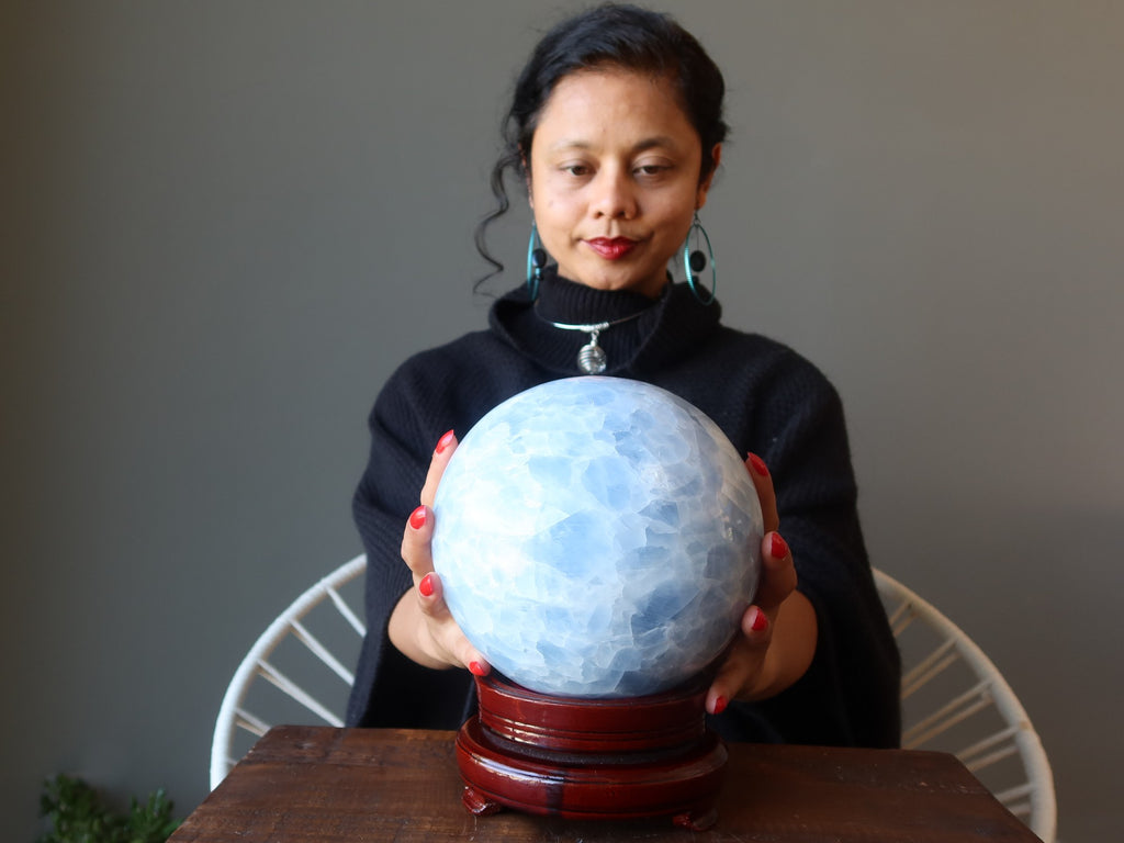 sheila of satin crystals with hands on a large blue calcite sphere