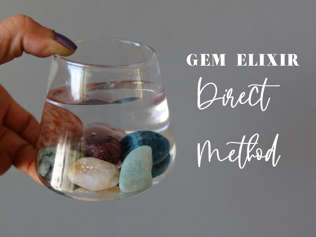 hand holding clear glass with stones in water for the direct method of gem elixirs