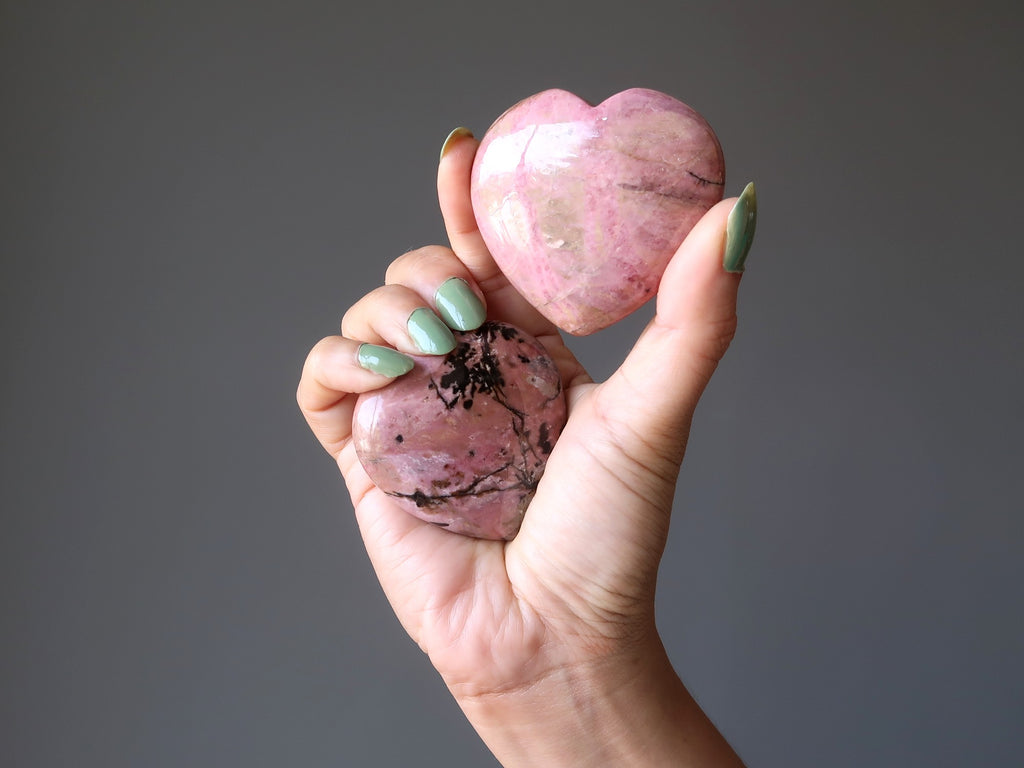 hand holding two pink and black rhodonite hearts