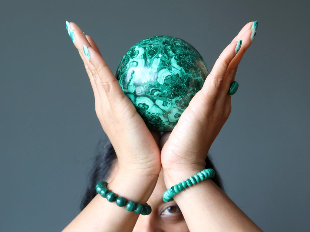 Sheila of Satin Crystals holding up a Malachite sphere at her Crown Chakra