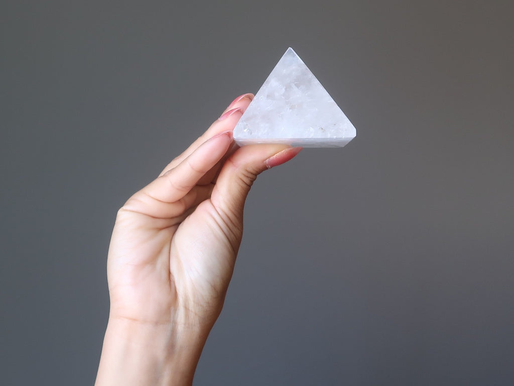 handing holding up at a clear quartz crystal healing pyramid