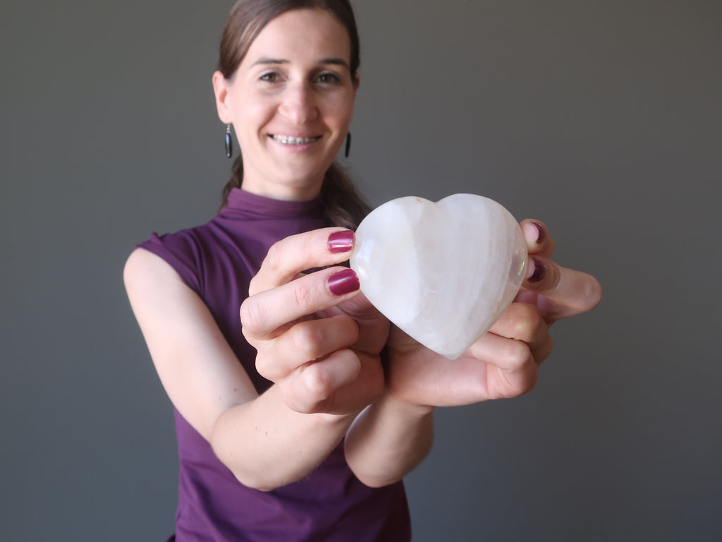 lucia of satin crystals holding up a quartz stone heart to open the chakra