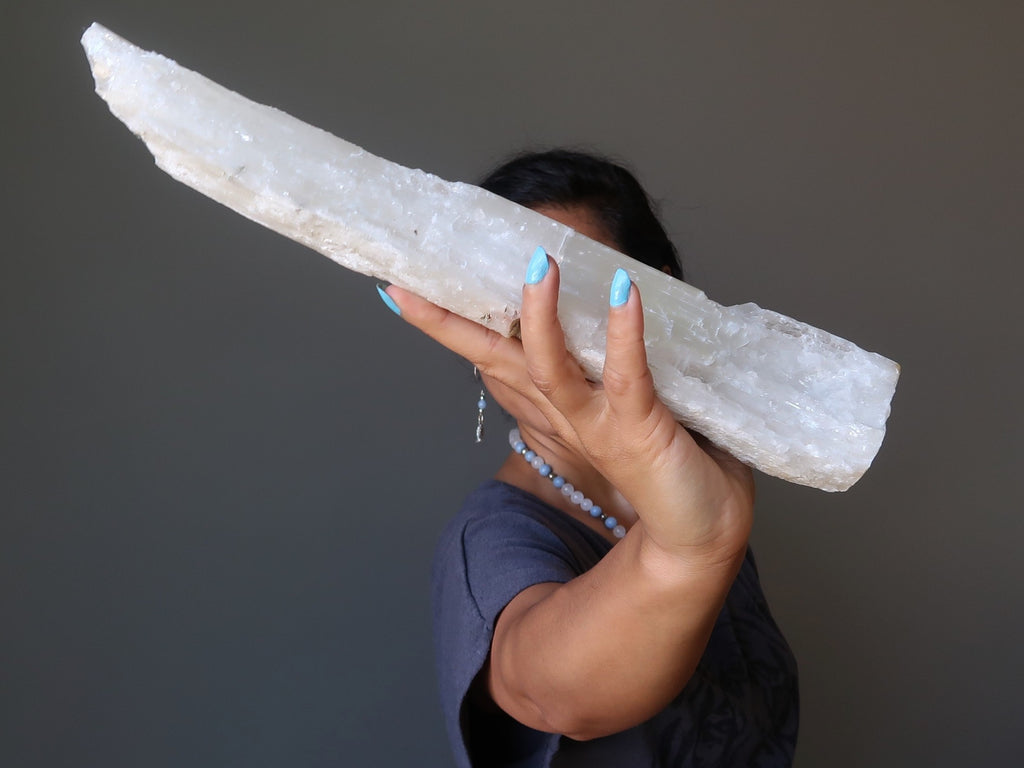 sheila of satin crystals holding up a large raw log of white selenite for the 4th dimension shift