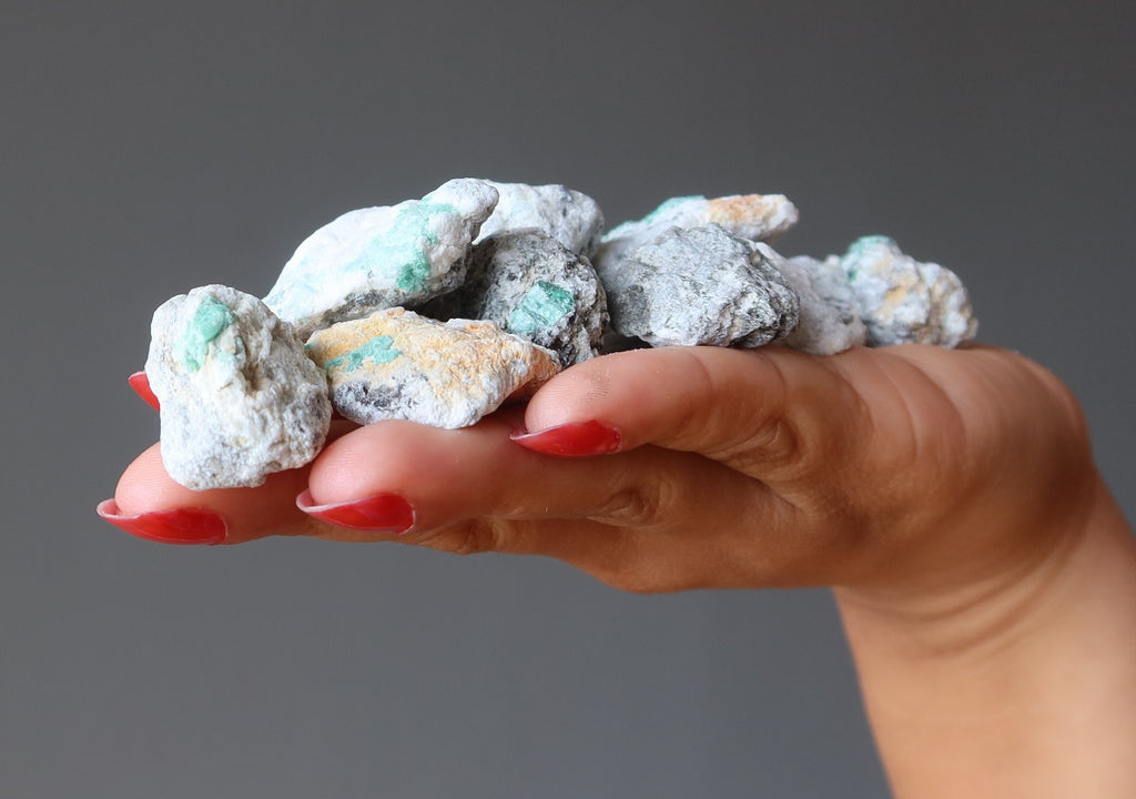 hand holding pile of raw emeralds