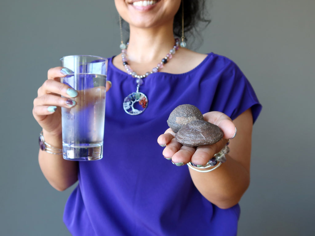 woman holding glass of water and pair of moqui marble stones