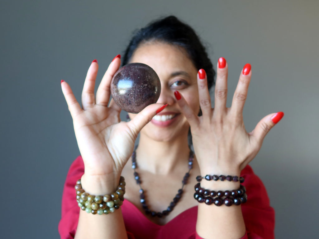 sheila of satin crystals wearing garnet jewelry and holding up a garnet ball