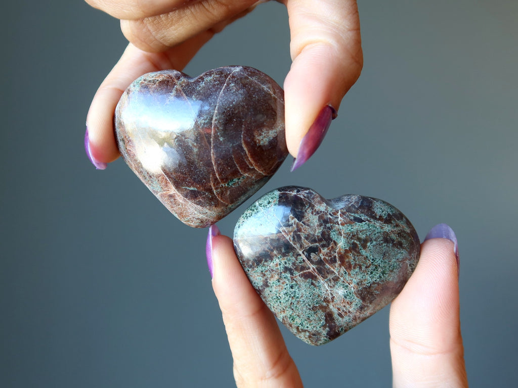 hands holding red and green garnet heart stones