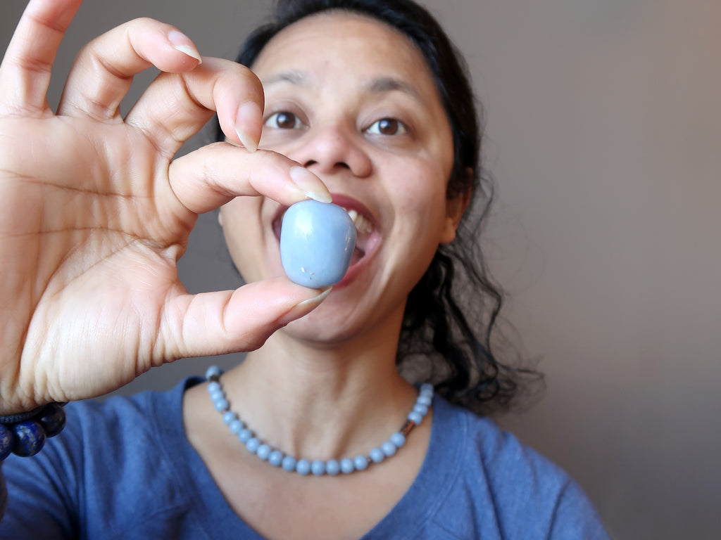 Satin Crystals owner holding blue angelite tumbled stone in front of her open mouth