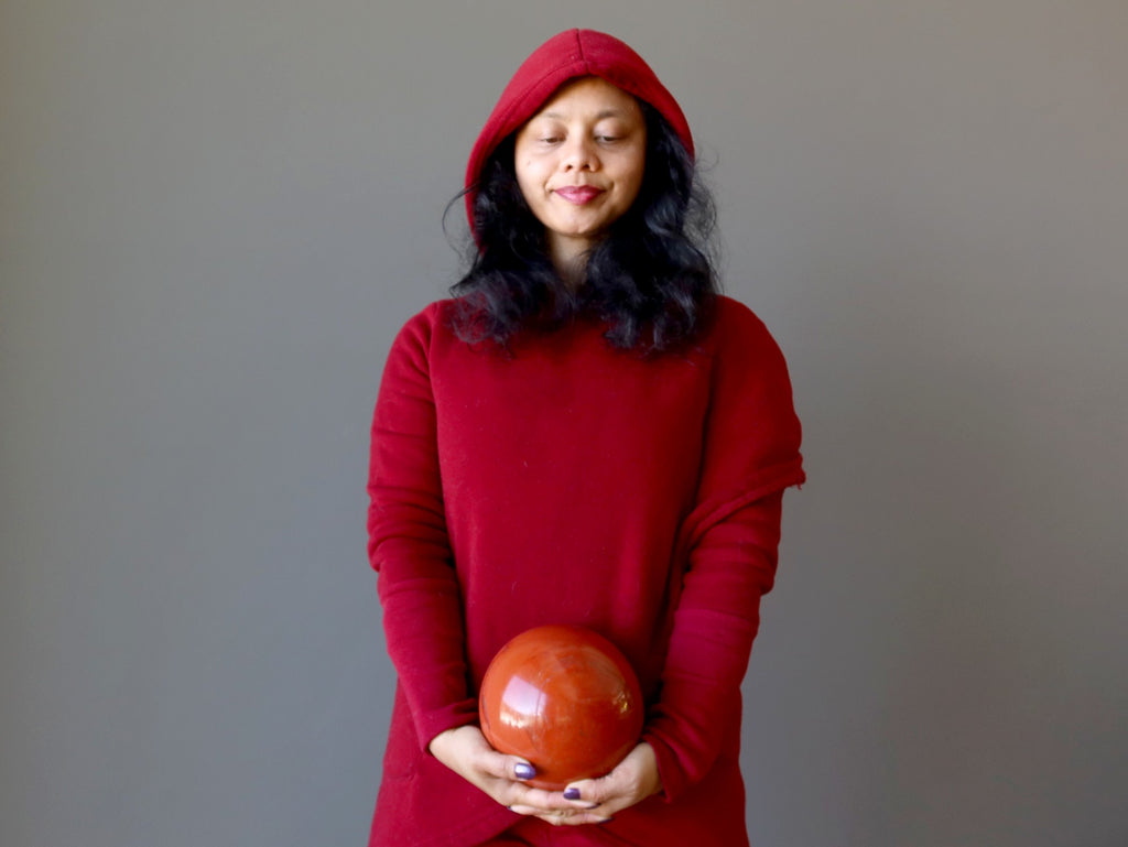 sheila of satin crystals in a red hoodie holding a red jasper ball at the root chakra