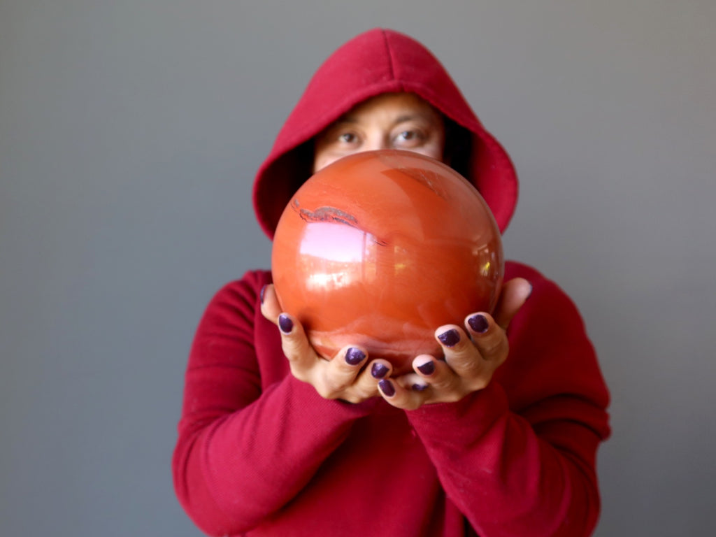 sheila of satin crystals in a red hoodie holding a red jasper ball