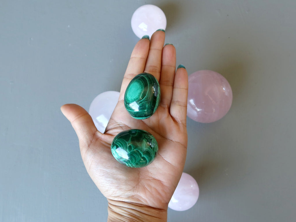 hand holding two malachite eggs over rose quartz spheres