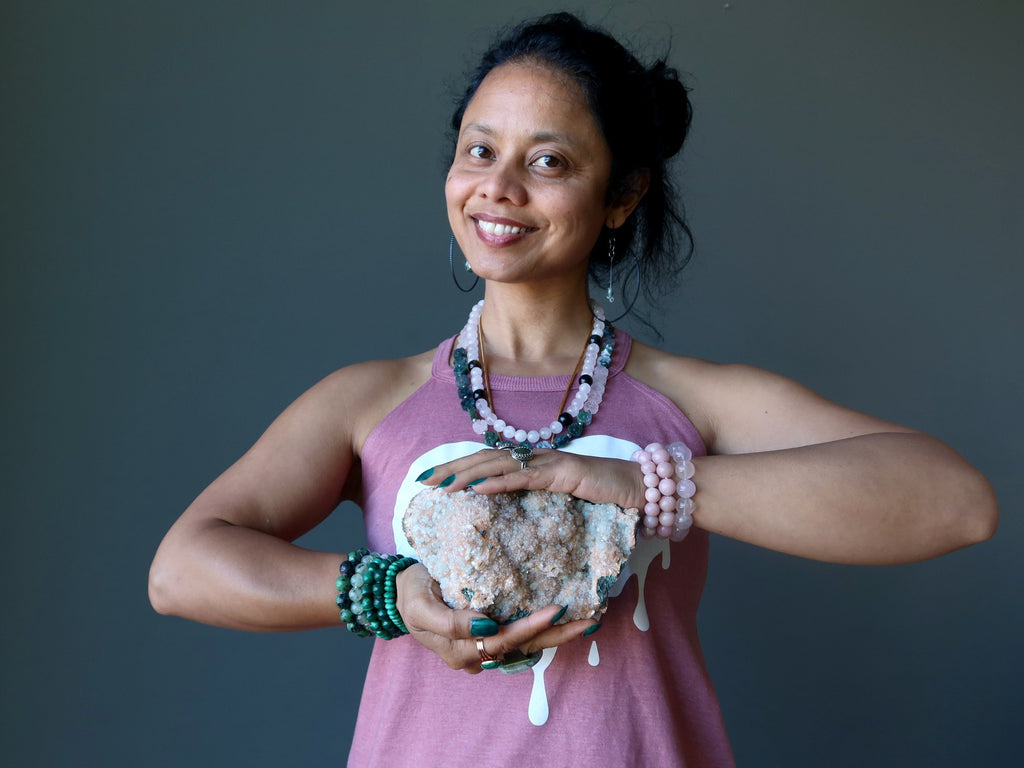 sheila of satin crystals wearing green and pink gemstone jewelry holding a stilbite cluster at her heart chakra