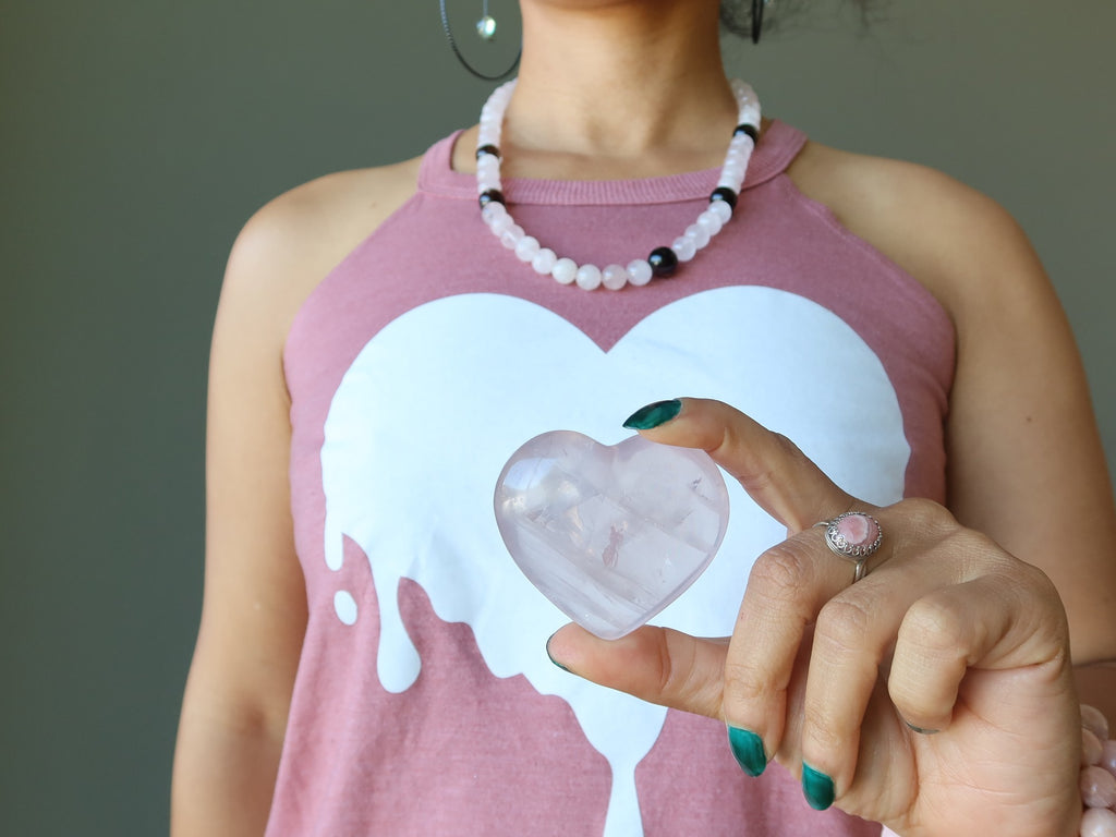 rose quartz heart held up against a white heart print on a pink tank top
