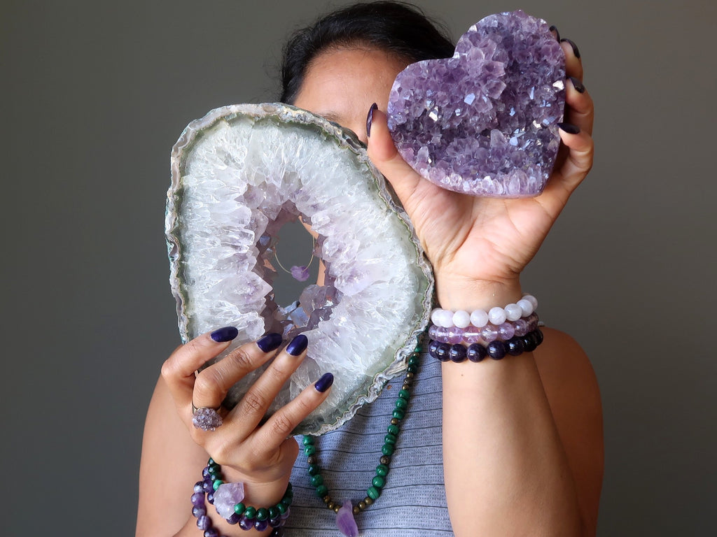sheila of satin crystals holding up an amethyst geode and purple amethyst cluster heart for the crown chakra