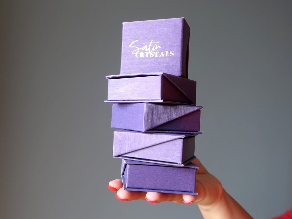 hand holding a stack of purple satin crystals boxes
