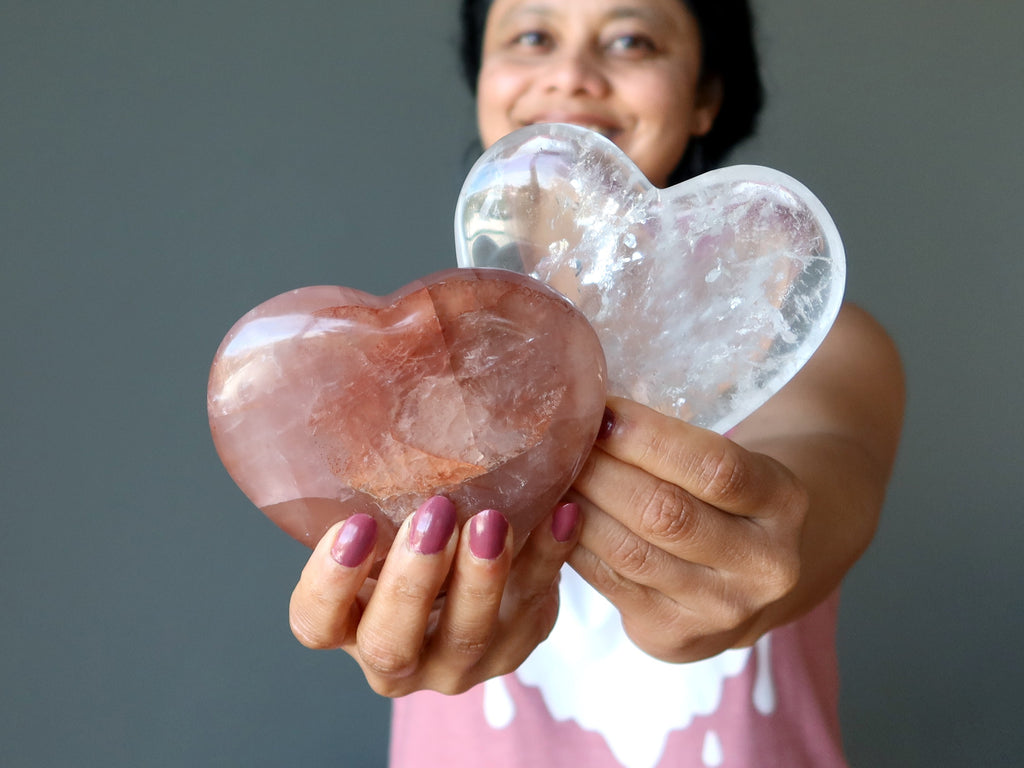 woman holding out a red and a clear quartz heart