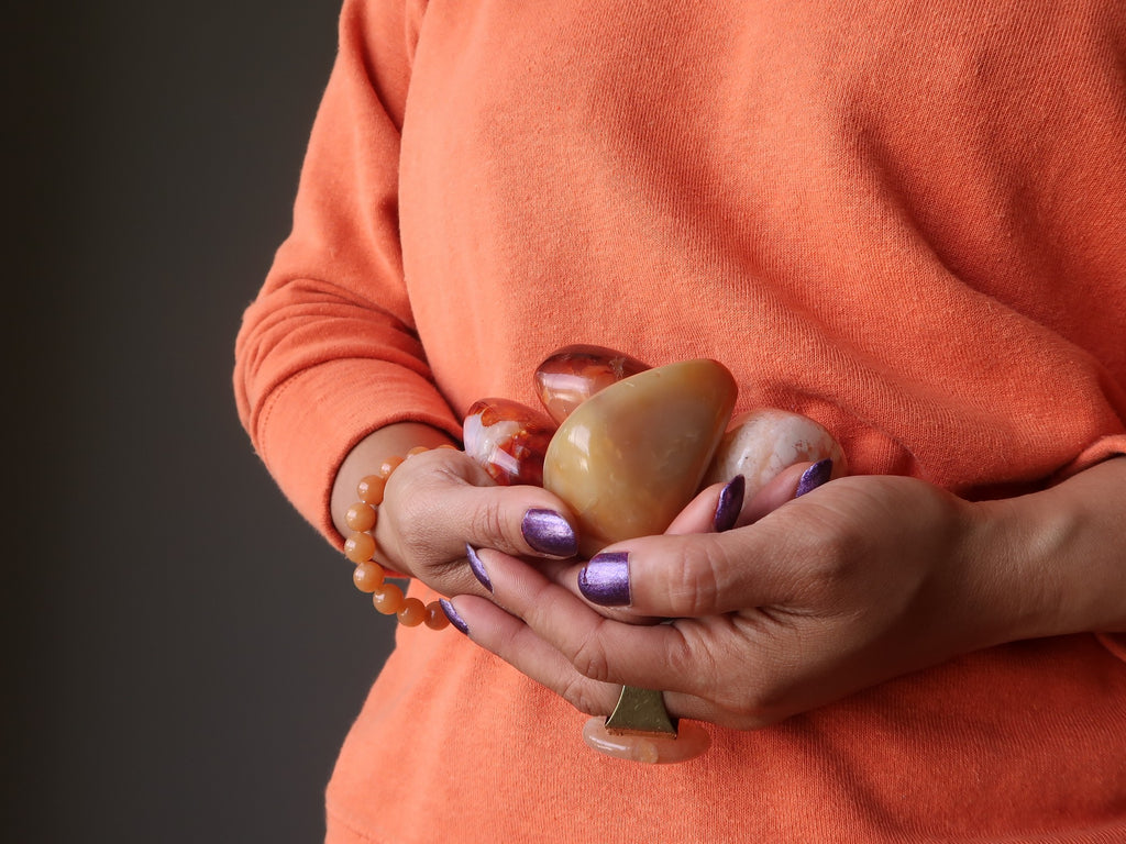 woman holding orange carnelian crystals to her belly