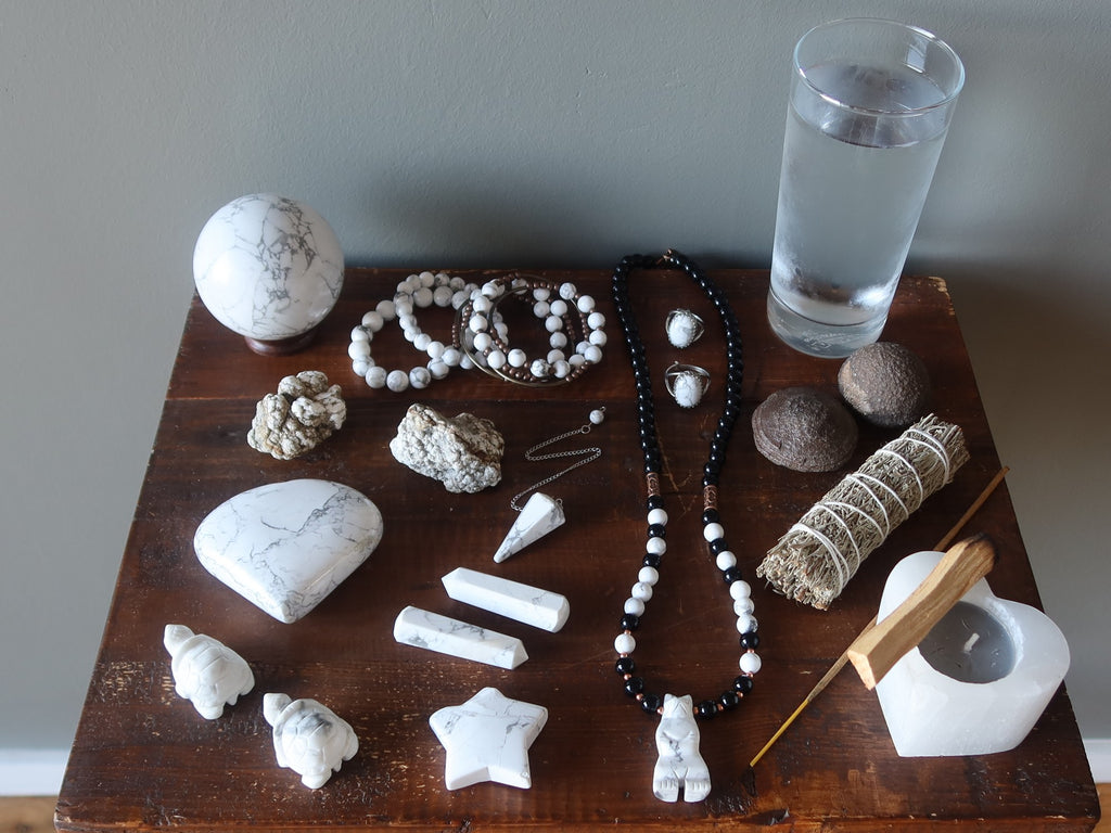 table of howlite stones and jewelry, glass water, moqui marbles, candle, sage