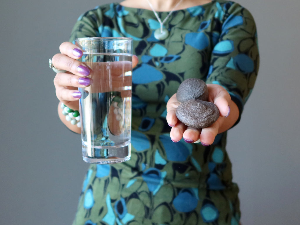woman holding glass of water and pair of moqui marbles